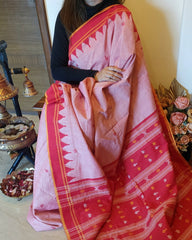 Person holding a pink and red saree with intricate patterns in a home setting.